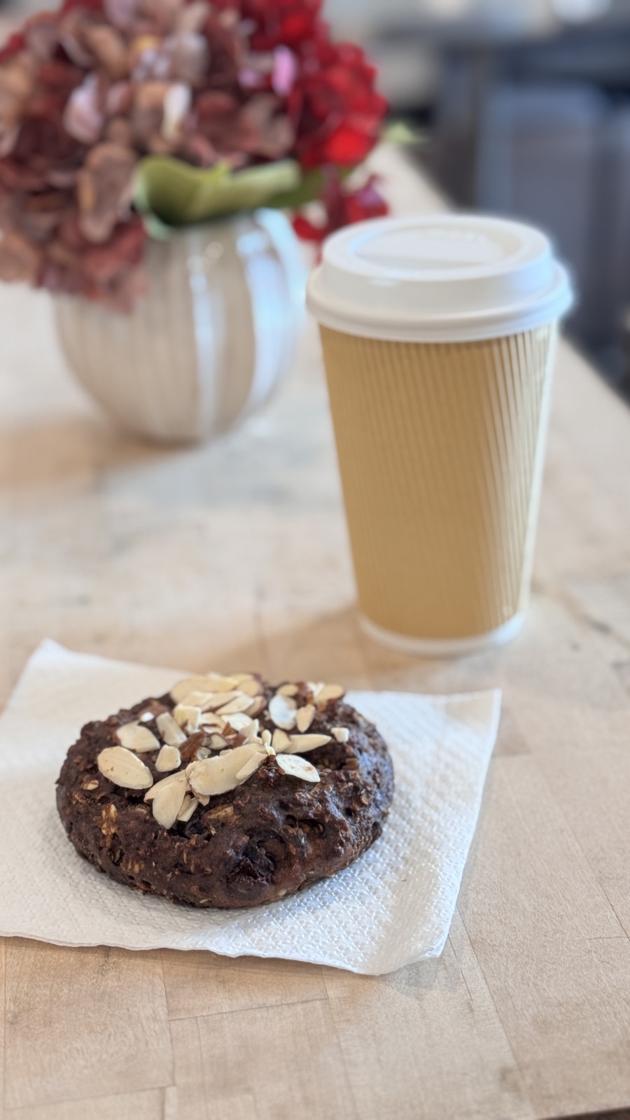 A cookie on a napkin next to a to-go coffee cup