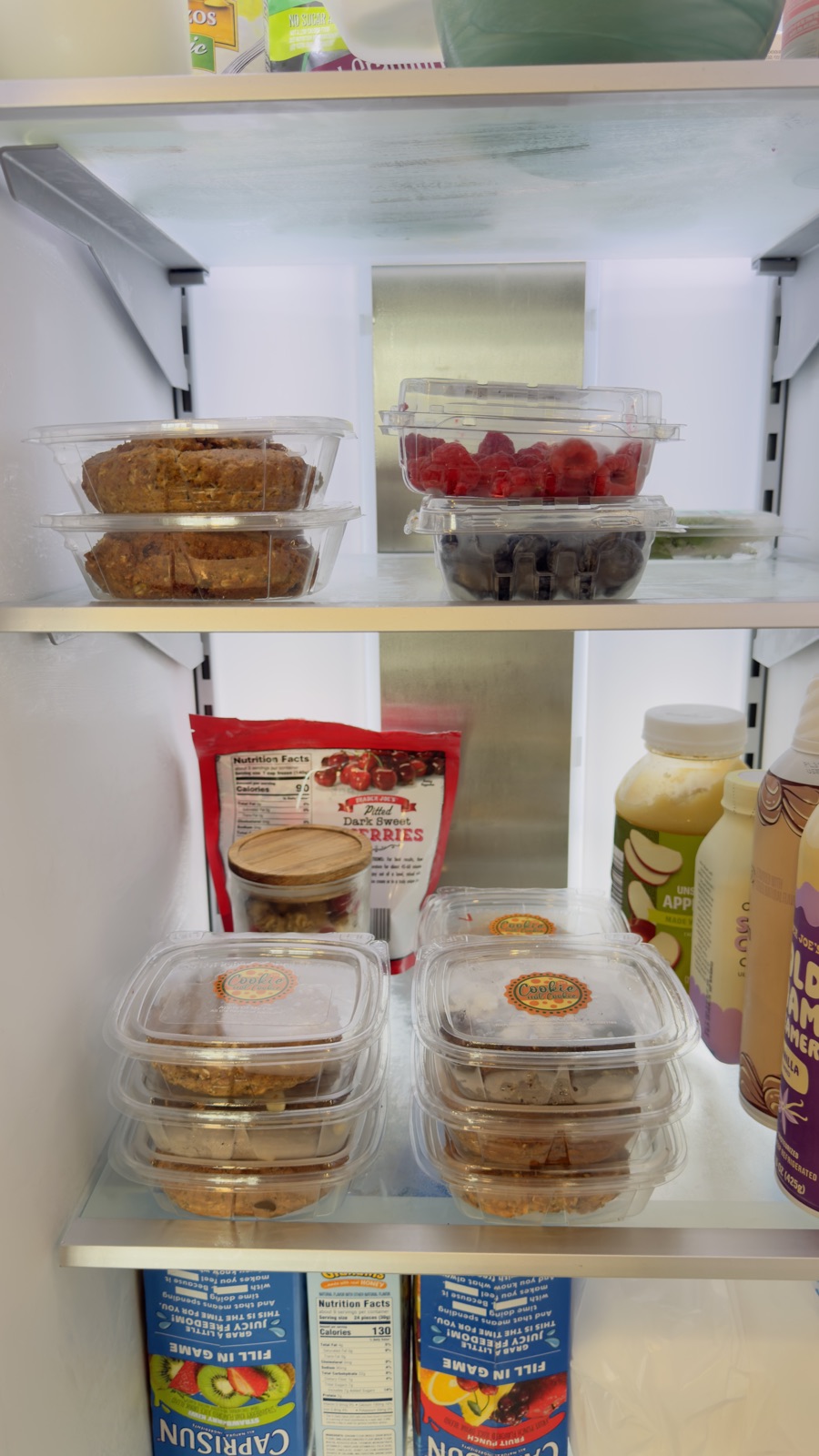 Refrigerator shelves stocked with Cookie Not Cookie containers beside raspberries, blueberries, and yogurt