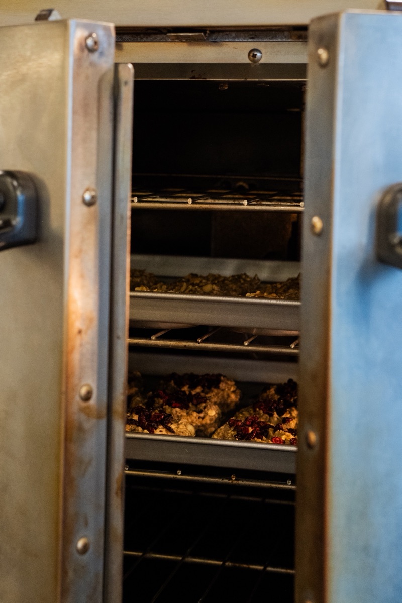 Open bakery oven with trays of oat clusters and cranberries mid-bake