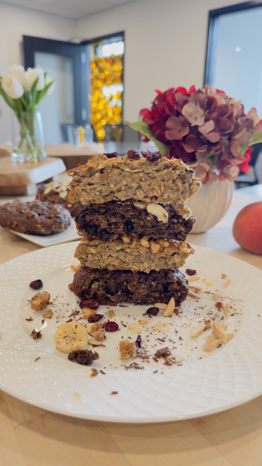 A stack of four broken-open Cookie Not Cookie halves on a white plate, soft interiors showing, with red hydrangeas and tulips behind